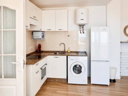 Modern kitchenette in Apartamentos El Calón Playa with white cabinets, granite countertop, washing machine, refrigerator, and