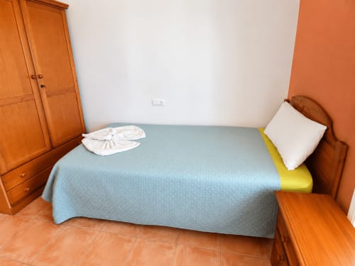 Bedroom with wooden wardrobe, blue bedspread, white pillow, and orange accent wall at Apartamentos El Calón Playa, Cuevas del