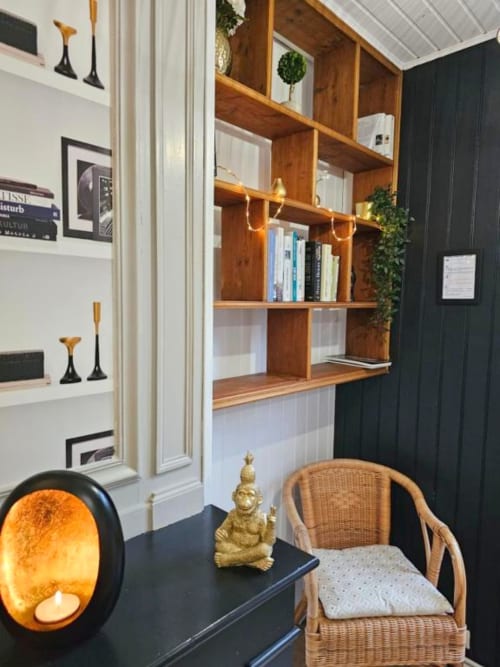 Espace de travail d'appartement moderne chez L'or Noir avec étagères en bois, bureau noir, chaise en rotin et statue de Bouddha dorée