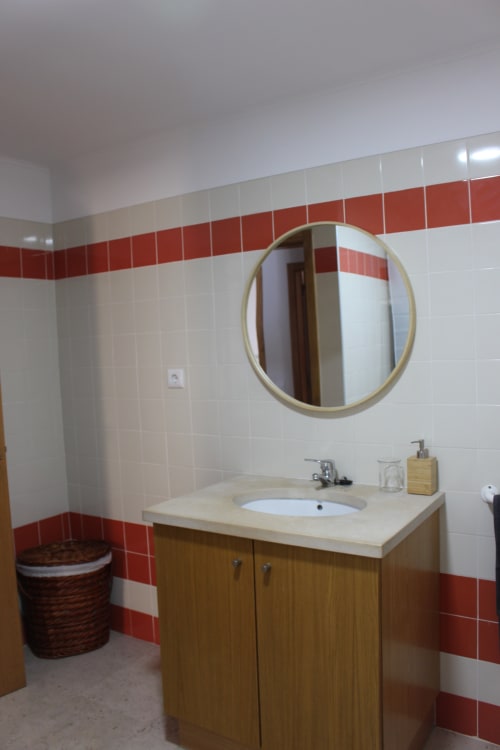 Modern bathroom with red and white tiles, wooden vanity, round mirror, and sink at Break Lovers in Tavira