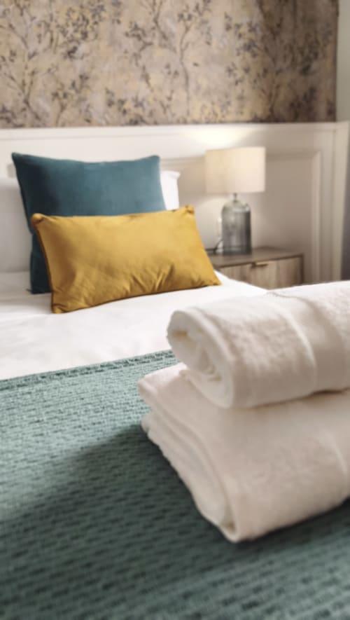 Dormitorio moderno en Mirador Medieval de Cáceres con almohadas amarillas y azul verdoso, ropa de cama blanca y alfombra de acento azul verdoso