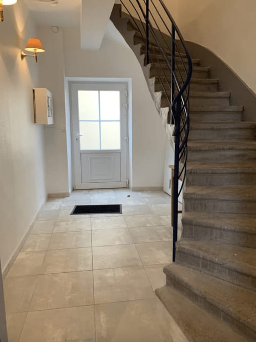 Entrée du gîte Le Restaurant du Port avec escalier en bois, porte blanche et carrelage