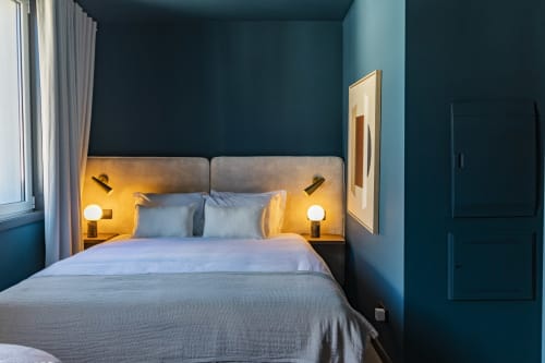 Moderno quarto estúdio compacto no hotel do Porto com paredes azul-petróleo, cama estofada cinza, iluminação aconchegante e vista da cidade