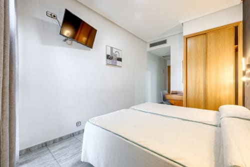 Habitación moderna en Hostal El Molino con camas gemelas, TV mural, armario de madera y paredes blancas en Collado Villalba