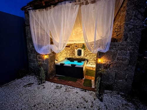 Luxueux bain à remous extérieur avec voilages vaporeux la nuit, murs en pierre, éclairage chaleureux, Domaine Valenquercy, France