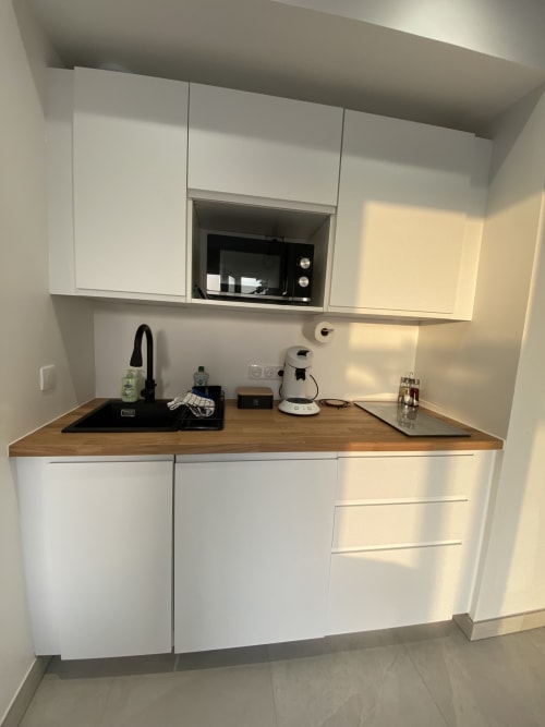 Kitchenette moderne du Studio 5 à La Maison Blanche avec mobilier blanc, plan de travail en bois, évier noir et cafetière