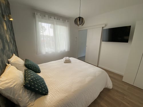 Chambre moderne de l'appartement La Maison Blanche à Bouguenais, literie blanche, coussins vert foncé, télévision murale et jardin