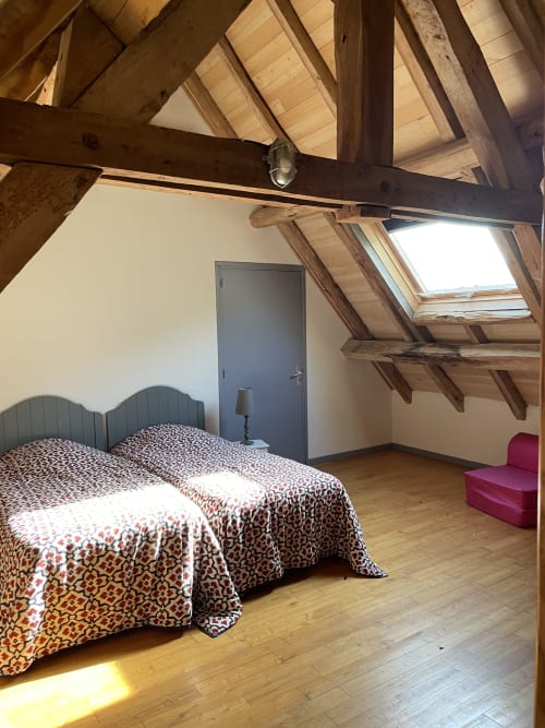 Chambre mansardée aux Chambres d'hôtes Les Pratges à Figeac : poutres apparentes, lucarne, parquet, literie à motifs