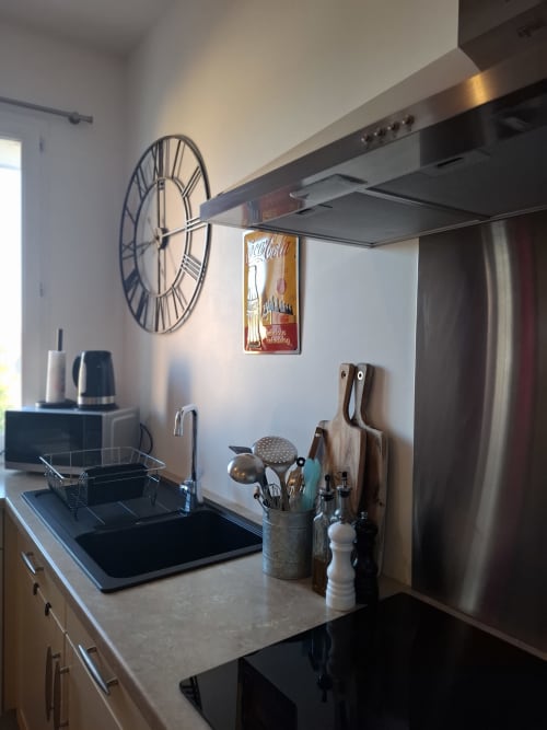 Cuisine moderne avec plaque de cuisson à induction noire, hotte inox, horloge murale décorative et ustensiles de cuisine chez Laure