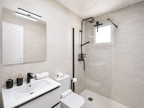 Modern bathroom at Apartamentos El Calón Playa with white sink, black fixtures, walk-in shower, mirror, and window