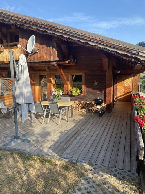 Chalet rustique en bois avec terrasse aménagée, parasol et coin repas à La Ferme des Georgières à Notre-Dame-de-Bellecombe