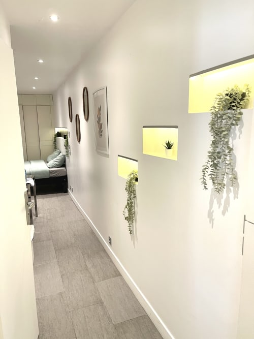 Couloir moderne de l'appartement Le Paradis Des Logis à Saint-Brice-sous-Forêt : murs blancs, plantes suspendues, lumière jaune chaleureuse.