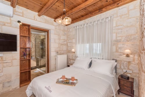 Luxury villa bedroom in Kokkino Chorio, Crete with stone walls, wooden ceiling beams, and modern amenities