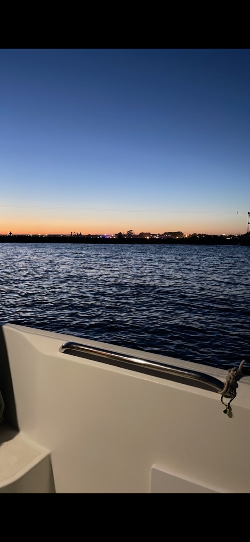Vue du coucher de soleil depuis un bateau à la marina de Cap d'Agde, propriété waterfront avec les lumières de la ville à l'horizon
