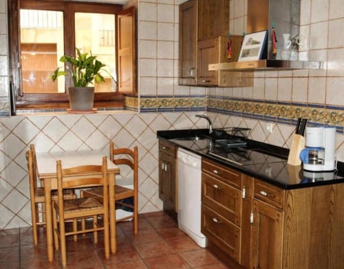 Cocina con muebles de madera, encimera negra, estufa y comedor en el apartamento Casas Rurales La Viña, Cuzcurrita de Río