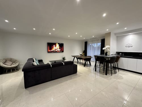 Séjour moderne aux Gîtes Les Camelias 71 avec canapé noir, cheminée, cuisine et salle à manger