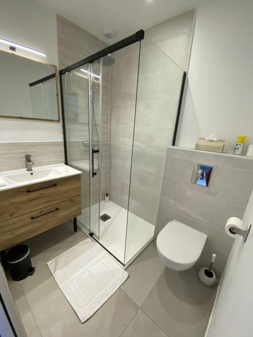 Salle de bain moderne de l'appartement La Maison Blanche avec douche, toilettes, meuble-vasque en bois et carrelage beige à Bouguenais