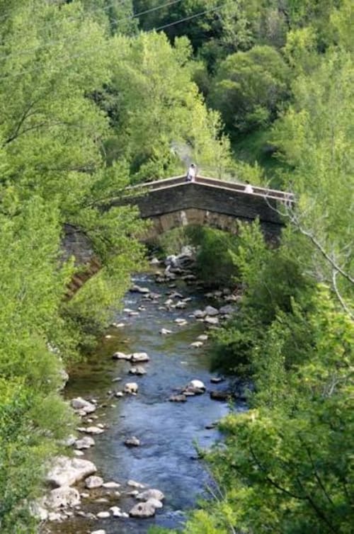 Puente de piedra sobre un arroyo de montaña rodeado de frondosos árboles verdes en los Prepirieos, cerca de Montgat