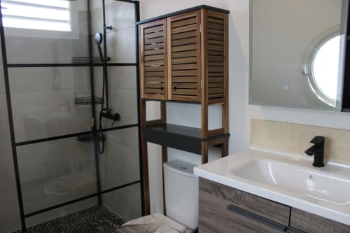 Salle de bains moderne avec douche à l'italienne, lavabo blanc, robinetterie noire, meuble de rangement en bois et miroir rond à Maisons En Or