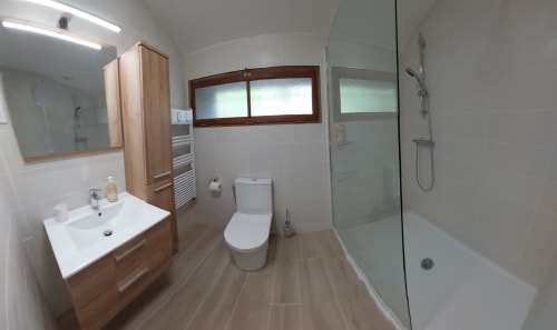 Modern bathroom at Les Gites de Campardon with white sink, toilet, and walk-in shower with glass enclosure