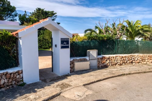 Entrada a apartamento Las Golondrinas con arco blanco, rótulo y muros de piedra en propiedad Cap d'Artrutx
