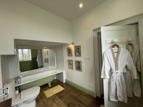 Salle de bain moderne du Château de Vaux Morvan avec mur d'accent vert, grand miroir, parquet et peignoirs blancs