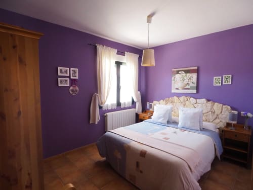 Dormitorio luminoso en tono púrpura del apartamento Senda del Duratón en Sebúlcor, con cama queen, muebles de madera y ventana con vista al jardín