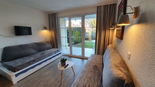 Modern apartment living room at Ô CAP COZ in La Fôret-Fouesnant with sofa, armchair, sea view through glass doors, and warm