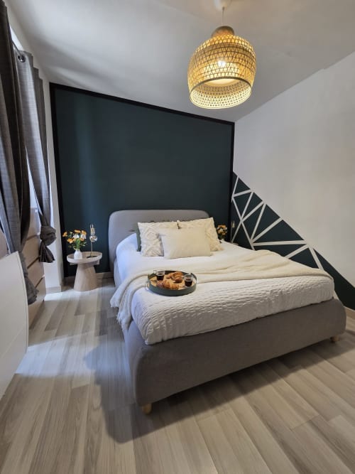 Chambre moderne à la Residence Cosy à Saint-Méen-le-Grand avec lit gris, mur d'accent noir, luminaire suspendu tressé et éléments bois