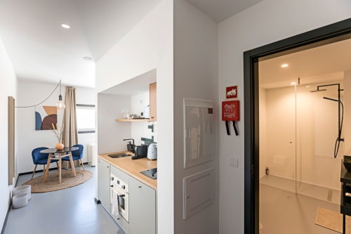 Estúdio moderno com kitchenette, cadeira azul e chuveiro de vidro no hotel Benefit Collection no Porto