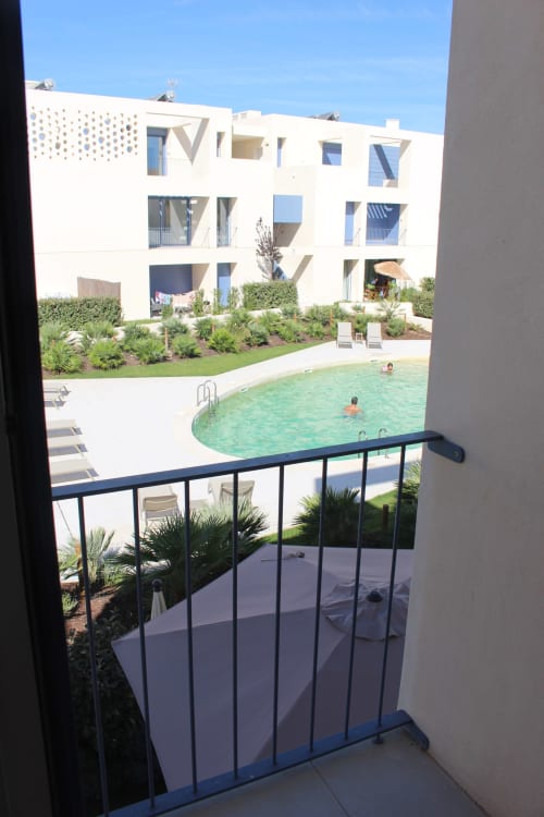 Balcony view of curved pool at Break Lovers apartment in Tavira, Portugal with white building and landscaping