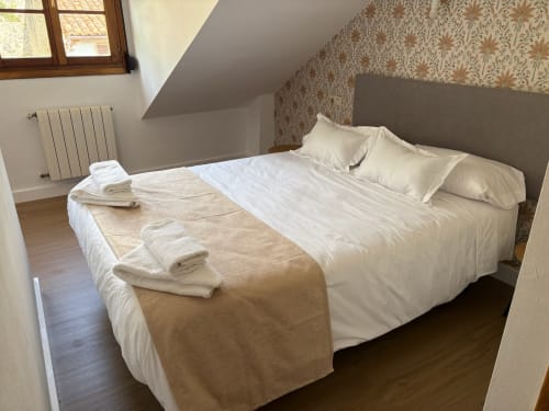 Habitación doble en Pensión Argüelles de Ribadesella con ropa de cama blanca, manta crema y papel pintado floral