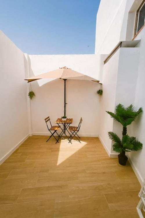 Patio privado con mesa de comedor de madera, sombrilla beige y plantas verdes en El HierroStay Apartments en La Restinga