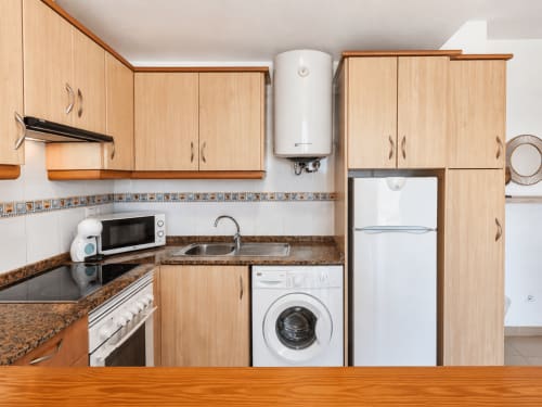 Cocina moderna con gabinetes de madera clara, encimeras de granito, electrodomésticos blancos incluyendo lavadora y refrigerador