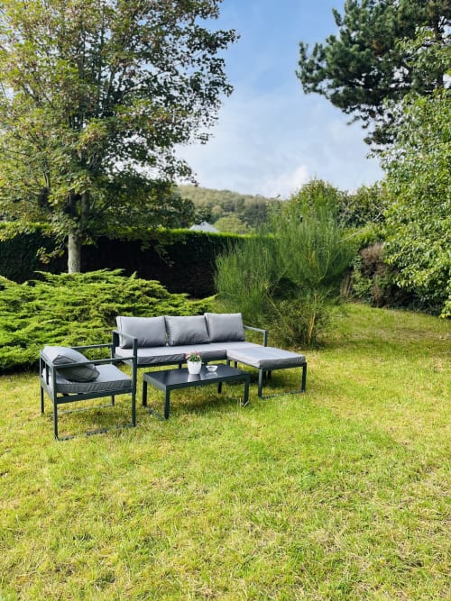 Mobilier de détente moderne avec coussins gris dans le jardin luxuriant du gîte ART DE VOYAGER à Étretat