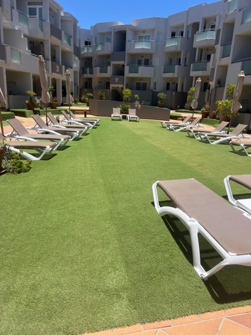 Sunny poolside courtyard at FTV Holidays Homes in Corralejo with lounge chairs and modern apartment buildings