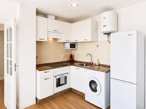 Modern white kitchen with granite countertop, stove, washing machine, and refrigerator in Apartamentos El Calón Playa, Cuevas