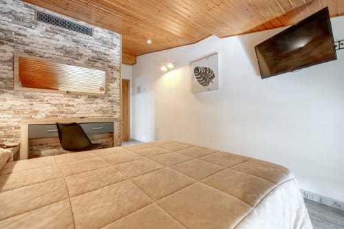 Moderno dormitorio doble en Hostal El Molino en Collado Villalba con techo de madera, pared de ladrillo, escritorio, TV y colcha acolchada