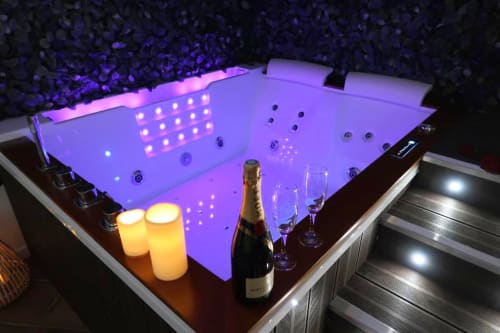 Baignoire balnéo luxueuse aux Gites Saint Valery En Caux, illuminée de lumières LED rose et violet, champagne et verres à proximité