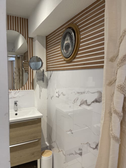 Salle de bain moderne à La Montagnette avec douche en marbre, touches de bois, miroirs ronds et sanitaires blancs
