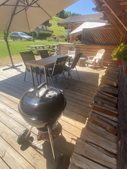 Terrasse en bois à La Ferme des Georgières avec barbecue, table à manger, parasol et vue sur les montagnes