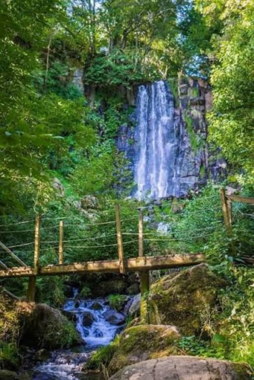 Cascade majestueuse encadrée de verdure luxuriante avec passerelle en bois enjambant le ruisseau au Relais de La Mirpe, Bergerac