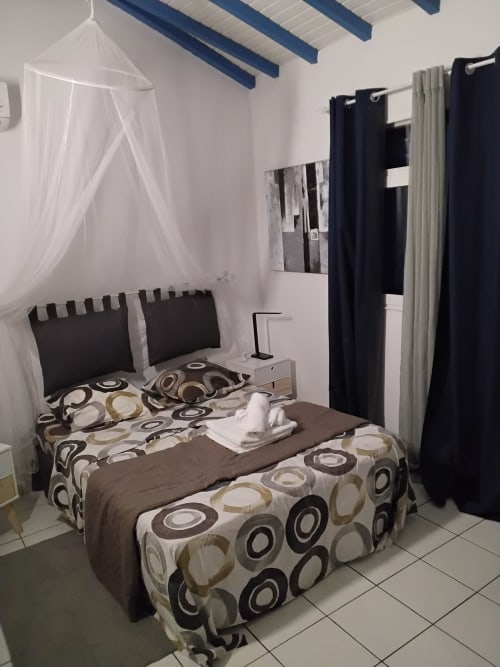 Chambre moderne de l'appartement Kay Betty aux Trois-Îlets avec lit à baldaquin, rideaux noirs et parure patterned