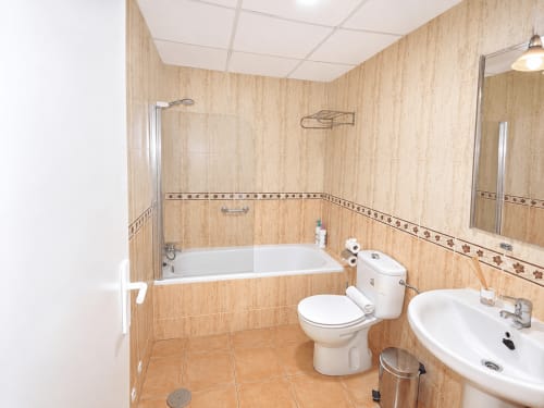 Modern bathroom with wooden tile walls, white sink, toilet, and bathtub at Apartamentos El Calón Playa, Cuevas del Almanzora