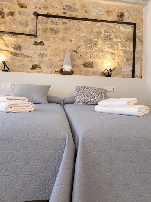 Habitació lluminosa amb dos llits, paret de pedra i gnom decoratiu a L'Algars boutique hostal de Tarragona