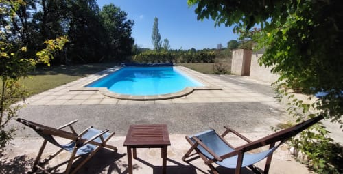 Sunflowers cottage pool area with lounge chairs and table overlooking blue swimming pool surrounded by gardens at Les Gites