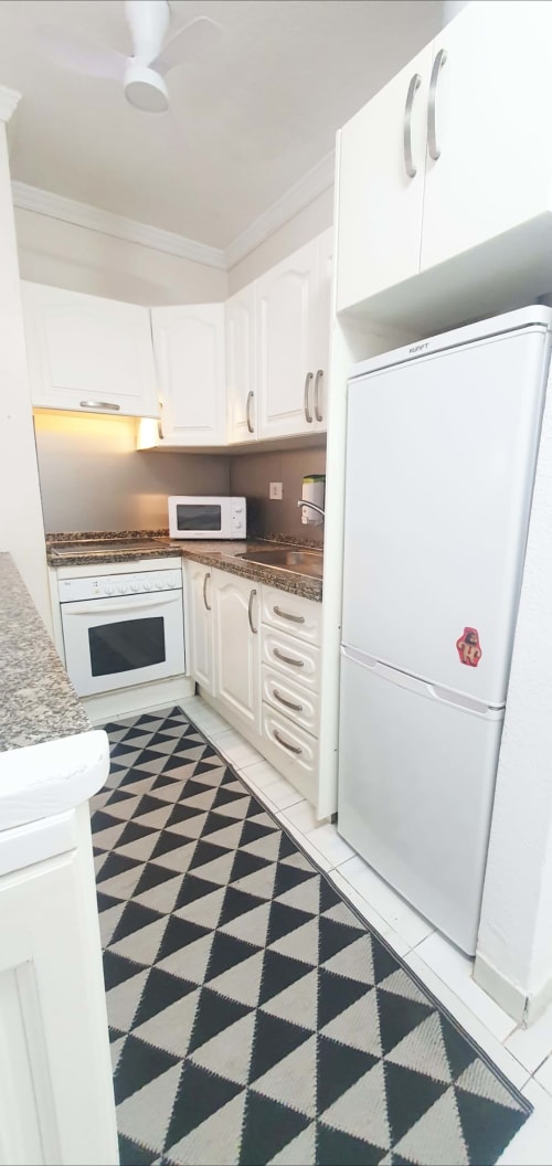 Cucina moderna bianca con piani in granito, elettrodomestici in acciaio inossidabile e piastrelle geometriche bianche e nere a Medano