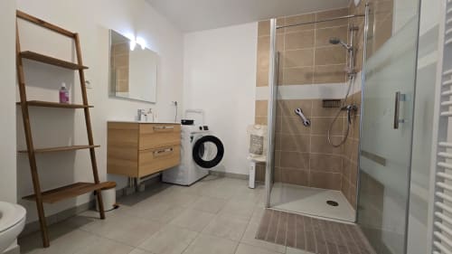 Modern bathroom with walk-in shower, wooden vanity, washing machine, and heated towel rack at Ô KASTEL apartment in La