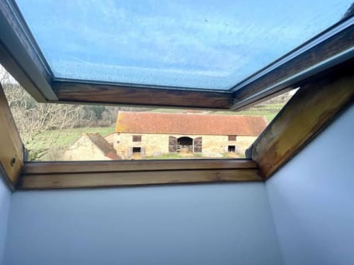 Vue depuis une fenêtre zénithale sur la grange historique en pierre avec toit en terre cuite du Château de Vaux Morvan, Étang sur Arroux