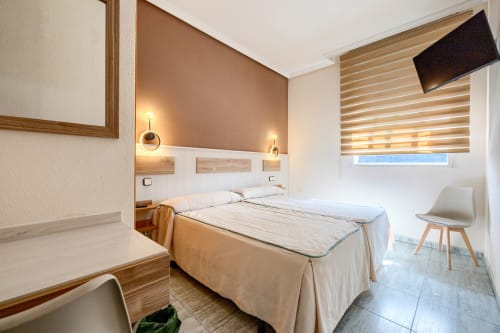 Moderna habitación doble en Hostal El Molino, Collado Villalba, con camas gemelas, detalles de madera, apliques de pared y TV